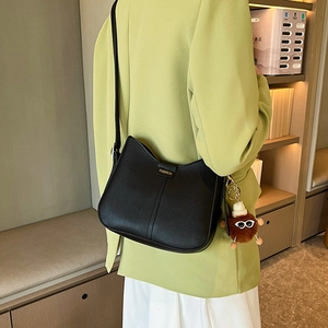 Black matte leather bucket bag with gold logo and plush charm on a green blazer model