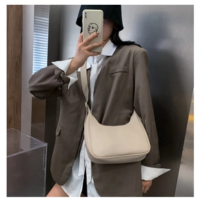 Close-up of a beige crescent hobo bag worn with a dark blazer for a chic retro style