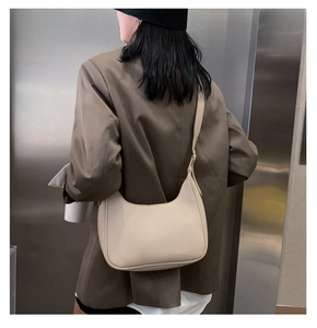 Adjustable shoulder strap detail on a beige crescent bag worn with a brown blazer