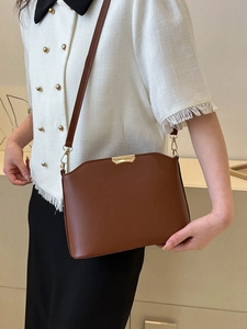 Braune Retro-Eimertasche aus Leder mit Goldbesatz an weißer Tweed-Jacke getragen