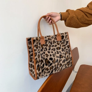 Faux fur leopard print tote bag with brown leather trim held in a cozy indoor setting