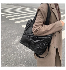 Close-up of black quilted puffer tote bag with side pocket shown in city street shot
