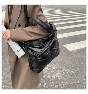 Close-up of black quilted puffer tote bag with glossy finish on a street background