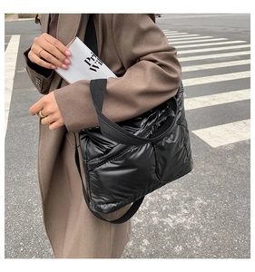 Modern black puffer tote bag worn cross-body with glossy quilted finish on urban street