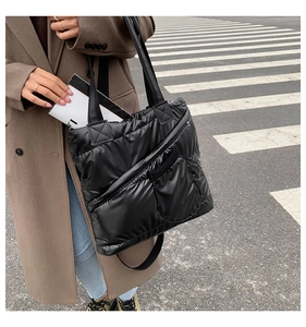Detail of black quilted down tote bag featuring functional front zipper pocket and wide strap