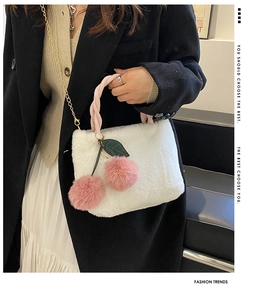 Detail of white plush cherry bucket bag featuring pink pompoms and gold chain strap