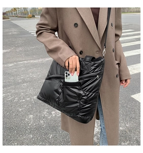 Outdoor shot of black quilted puffer tote showing front zipper pocket for smartphone