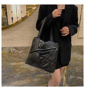 Detail of black quilted puffer tote bag featuring asymmetric zippers and glossy texture