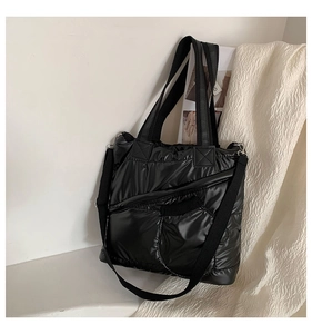 Detail of black quilted puffer tote bag with glossy nylon texture and crossbody strap