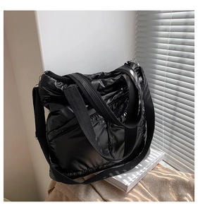 Close-up of black quilted puffer tote bag with glossy finish and wide straps in natural light