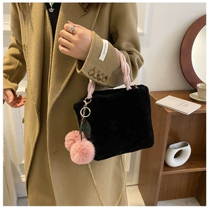 Detail of black plush handbag featuring pink woven handle and fluffy double pompom charm