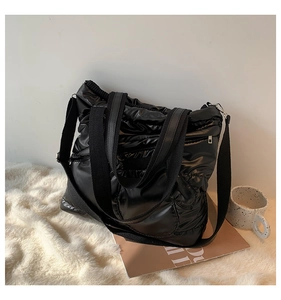 Detailed view of black quilted down tote bag with wide strap on a soft white carpet