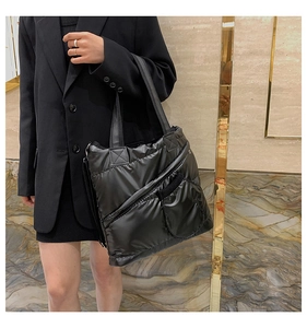 Detail of black quilted down tote bag with diagonal zipper pocket and wide strap