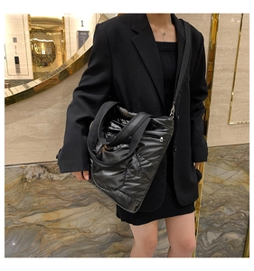 Detail of black quilted down tote bag with shoulder strap worn with a black blazer