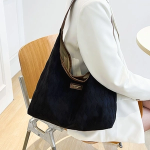 Sac cabas noir matelassé avec bordures en cuir marron porté à l'épaule dans un décor chic