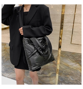 Detail of black quilted puffer tote bag with glossy finish and wide nylon shoulder strap