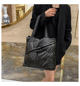 Detail of black quilted puffer tote bag with zipper shown on a model in a boutique