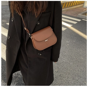 Brown leather saddle bag with metal trim shown on a model wearing a black coat