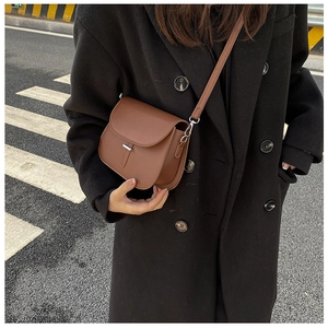 Close-up of a vintage brown saddle crossbody bag with silver buckle on a black coat