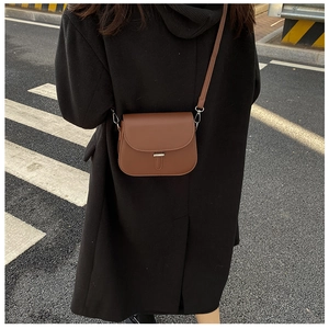Close-up of a brown leather saddle bag styled on a black coat in a street setting