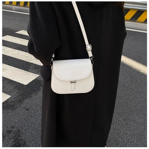 Close-up of a white minimalist saddle bag with metal clasp shown in street style