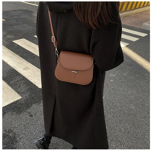 Close-up of a brown matte leather saddle bag worn with a black wool coat in the city
