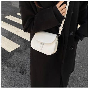 Close-up of white leather saddle bag with silver buckle worn over a black coat