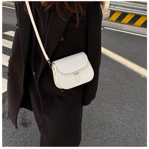 Close-up of a white vintage leather saddle bag with metal buckle on a street backdrop