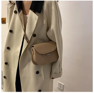 Close-up of khaki leather saddle bag with flap closure on model in beige coat