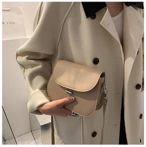 Detailed shot of a beige leather saddle bag with silver metal buckle on a model