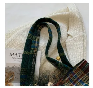 Detail view of the sturdy woven handle and green plaid tweed texture on the tote bag