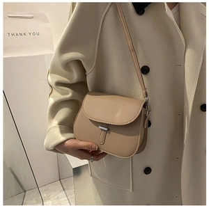 Detail of beige leather saddle bag with metal buckle worn by model in a minimalist style