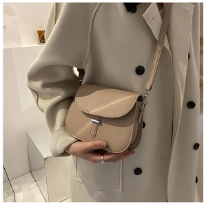 Detail of a beige leather saddle bag with silver buckle worn over an elegant coat