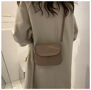 Side view of a minimalist apricot saddle bag with a metallic buckle on a female model
