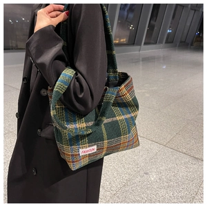 Detail shot of the green plaid tweed tote bag with a white fashion label on a model
