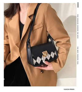 Detail of black and white checkered saddle bag with gold clasp on camel blazer