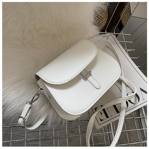 Close-up of white saddle bag with silver buckle on a plush background with a Vogue magazine