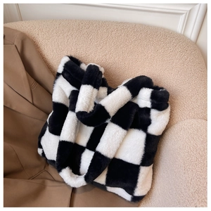 Detail view of the soft black and white checkerboard plush tote bag on a cozy chair