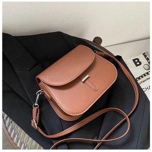 Detailed view of brown minimalist saddle bag with silver metal bar buckle on black fabric