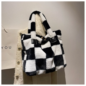 Detail of checkered plush tote bag hanging on a white tweed jacket with leather handles