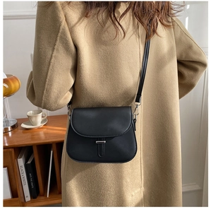 Close-up of minimalist black saddle bag with silver metal clasp on a beige coat
