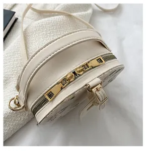 Detail of cream white round straw bag featuring smooth golden dual zipper and fine strap