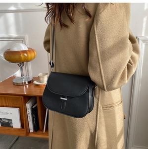 Close-up of a black vintage saddle bag with silver buckle worn by a model in a cozy room