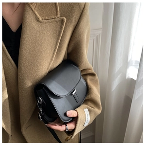 Detail of minimalist black saddle bag with silver T-shaped clasp on a wool coat