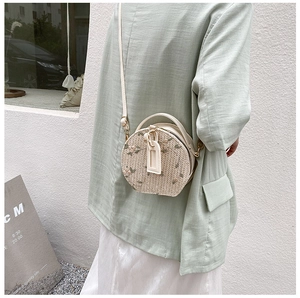 Detailed view of round straw bag with floral embroidery and top handle on a model