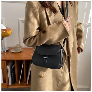 Close-up of a black vintage saddle crossbody bag with silver buckle on a wool coat