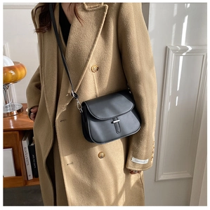 Close-up of minimalist black leather saddle bag with silver metallic buckle on a model