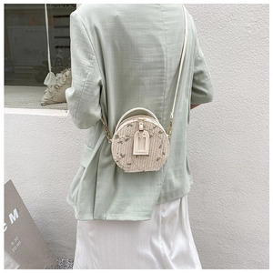 Close-up of small round straw bag with floral embroidery and white leather strap