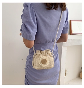 Detailed back view of a beige straw crossbody bag with a daisy flower decoration
