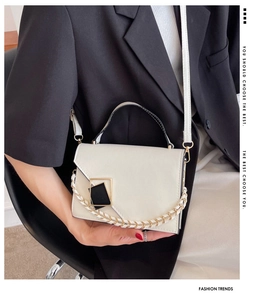 Detail of cream-white crossbody bag with gold-accented chain and metal hardware buckle